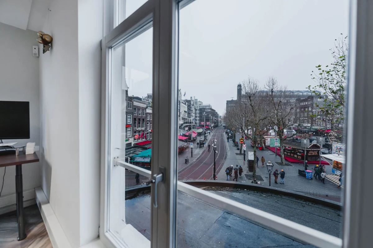 Uitzicht vanuit een raam op de drukke Korte Reguliersdwarsstraat in Amsterdam met winkels, marktkramen en voorbijlopende mensen.